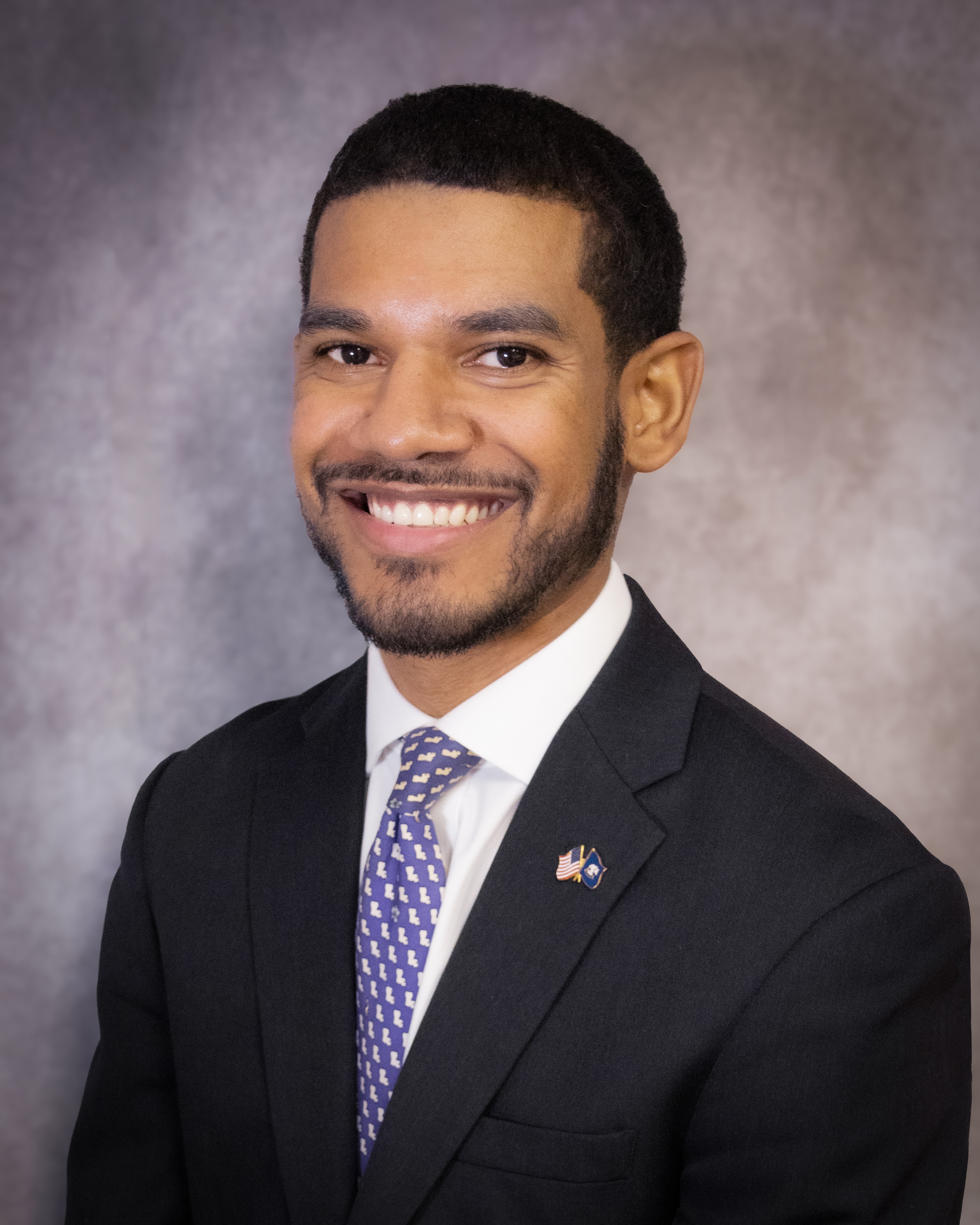 Dustin Davidson, in a professional headshot, wearing a suit and tie against a neutral background.