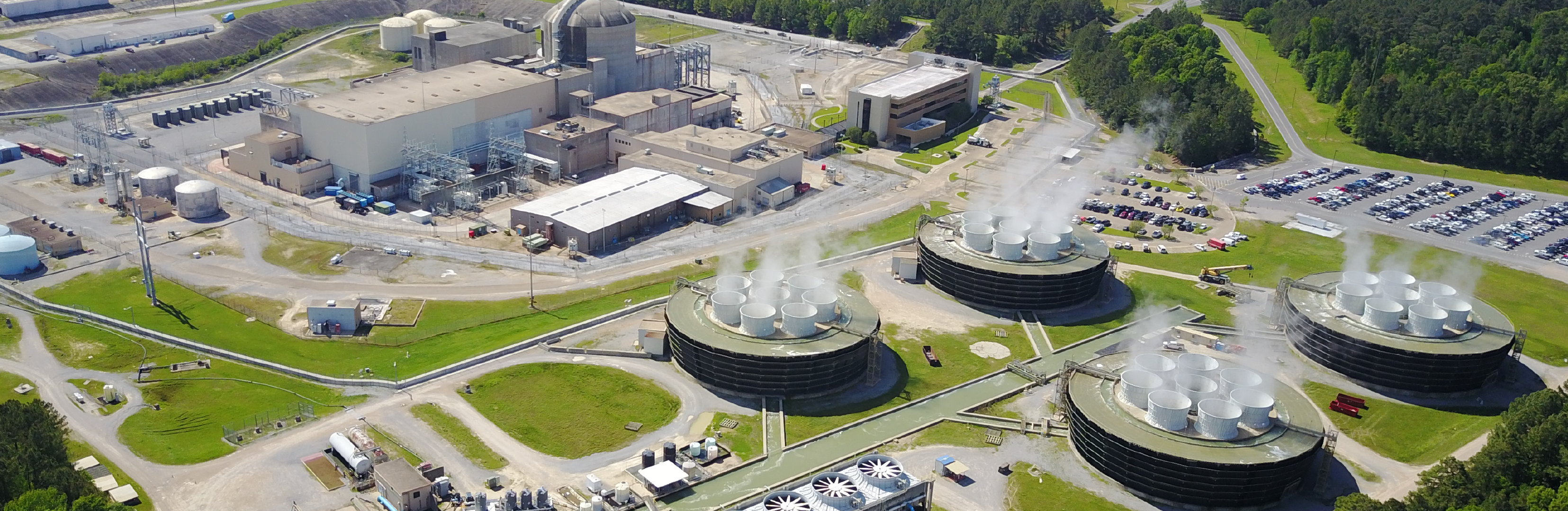 Aerial view of River Bend Nuclear Generating Station in St. Francisville, showing a domed reactor building, multiple circular cooling towers releasing white steam, surrounding industrial structures, w